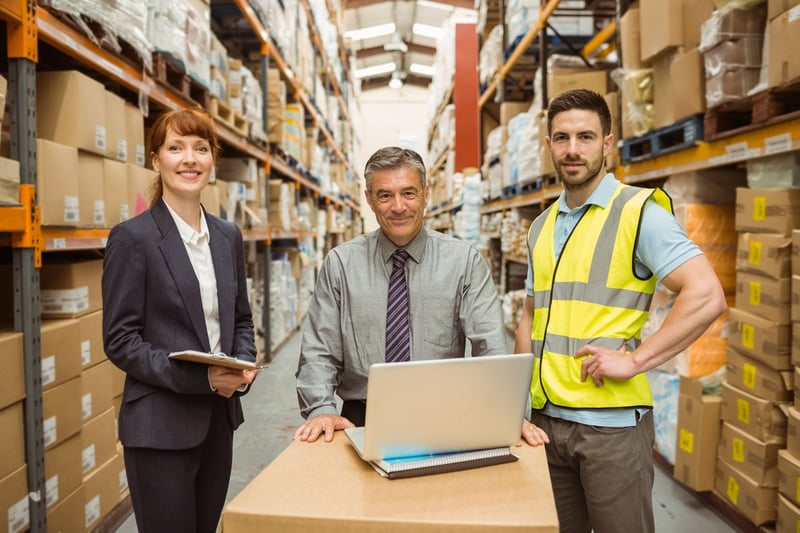 Smiling warehouse team working together on laptop in a large warehouse